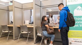 female student sits and chair and talks to standing male student at the LASC Financial aid counter.
