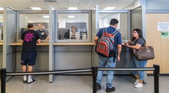 male student speaks to financial aid clerk while another male and female student have a conversation nearby